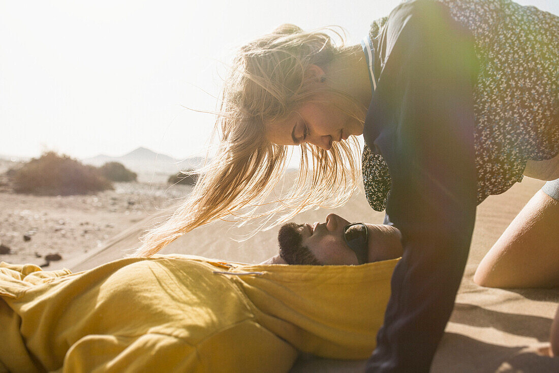 Romantic young woman looking at man lying on sand