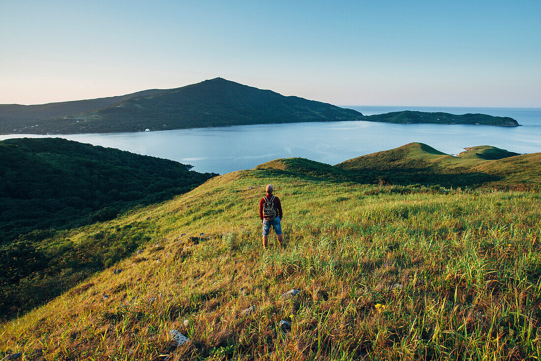 Rear view of hiker standing on grassy field while looking at East sea against sky