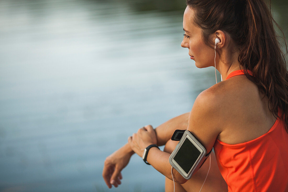 Rear view of woman sitting by pond while listening to music at park