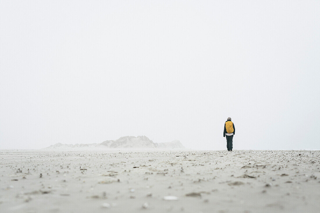 Rear view of female hiker walking on field against sky in foggy weather