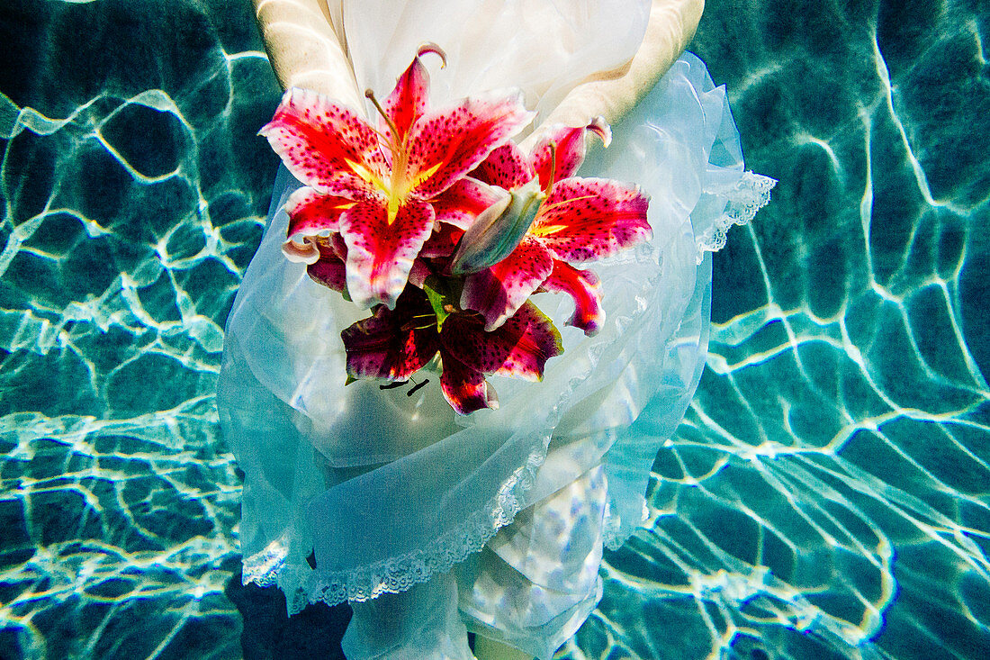 Caucasian woman wearing dress holding bouquet of flowers underwater