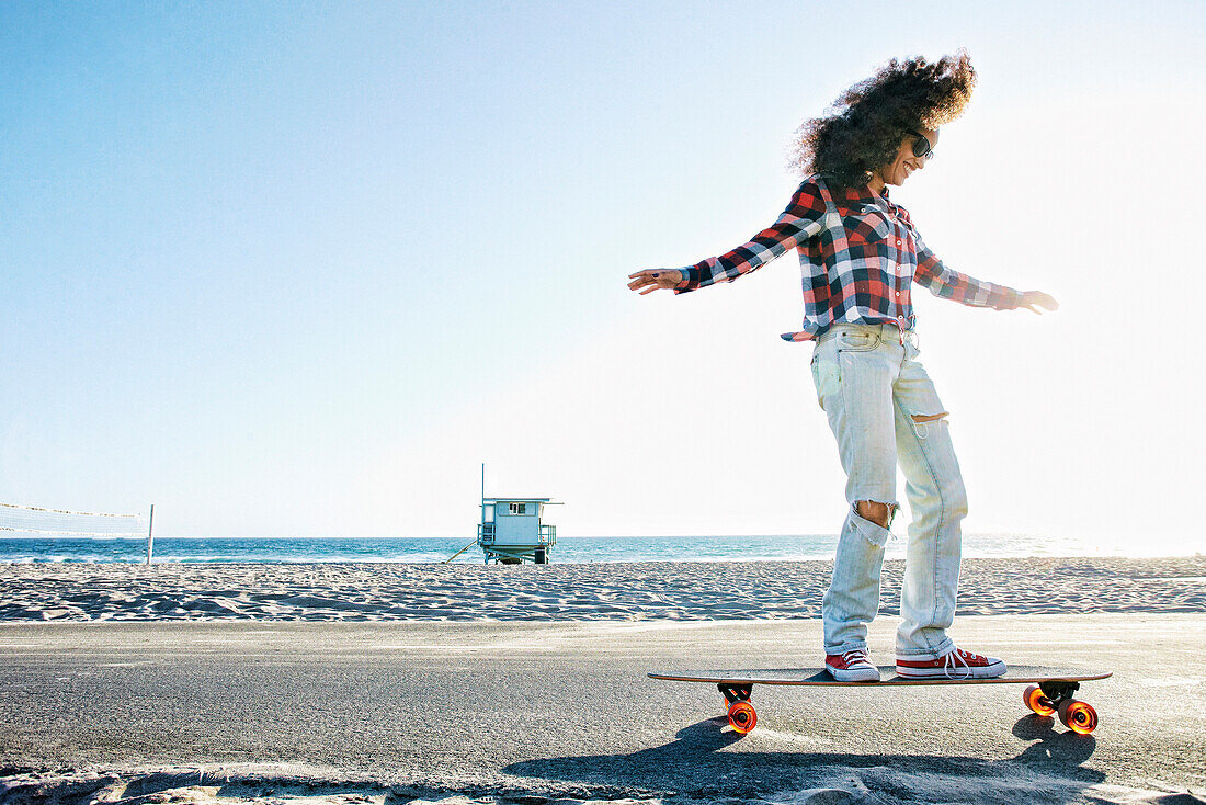 Hispanic woman riding skateboard at beach