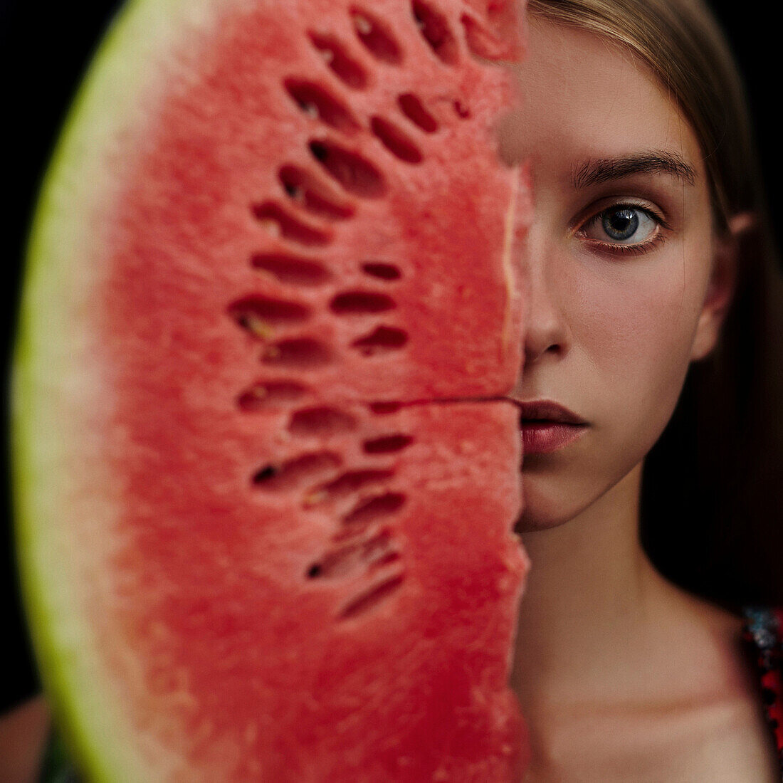 Caucasian girl holding slice of watermelon over half of face