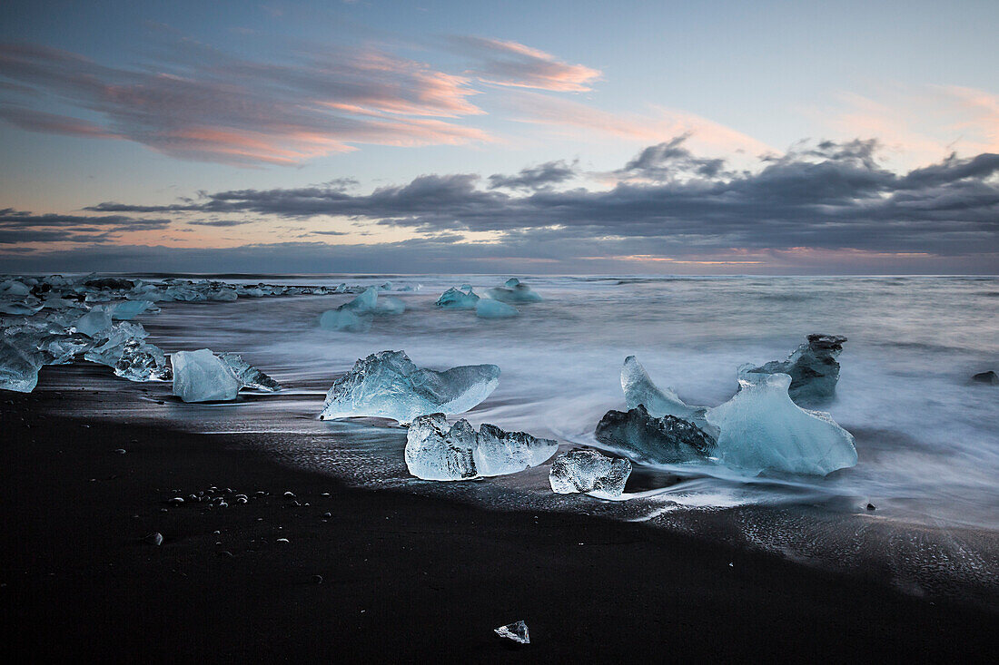 A winter sunset from Jokulsarlon black beach in southern Iceland, depicted at long exposure to enhance the wave motion and pattern