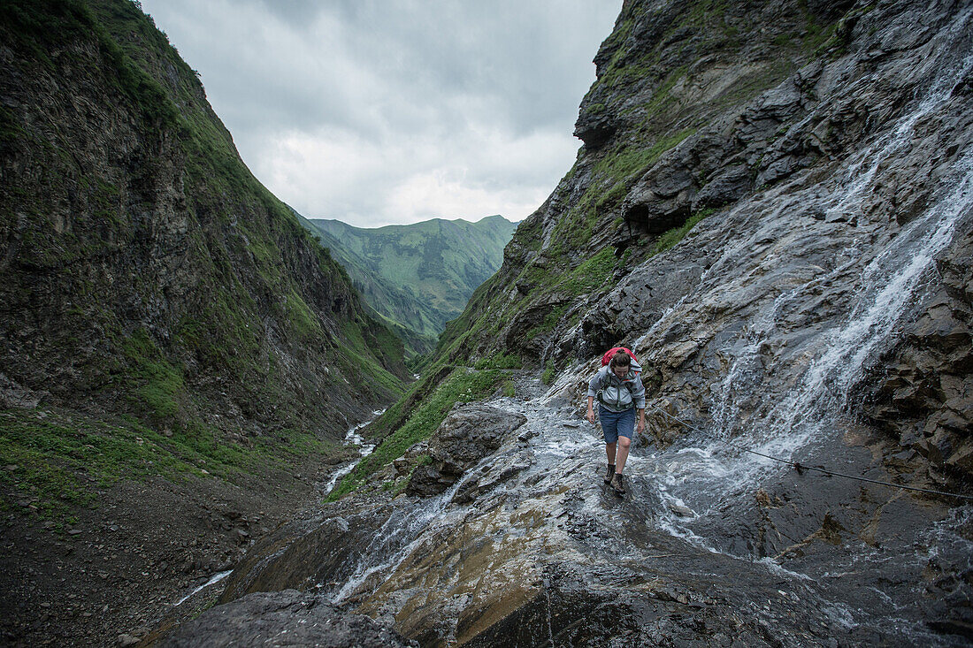 Young woman hiking past a small waterfall to the Kemptener Hütte in the Alps