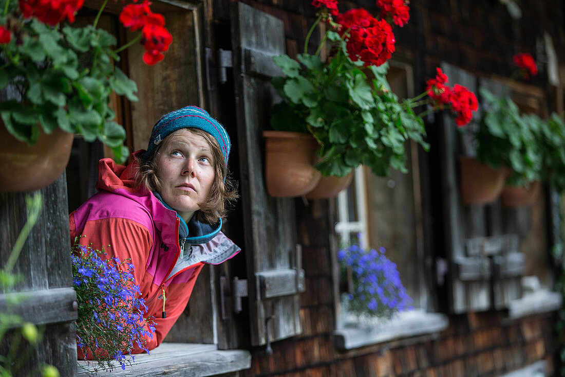 Young woman looking out of a window of the Kemptener Hütte in de Alps