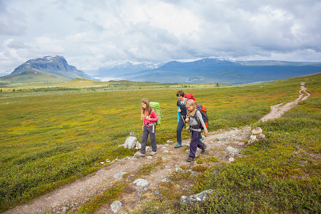 Two girls and one woman hike on the Kungsleden trekking, stage Saltoluokta to Sitojaurestugorna. Laponia, Lapland, Sweden.