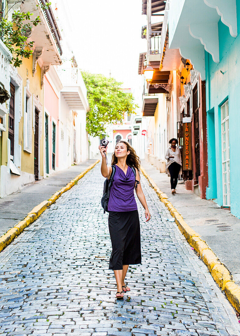 Young Woman Taking Picture Of Cobblestone Street Surrounded By Colourful Buildings