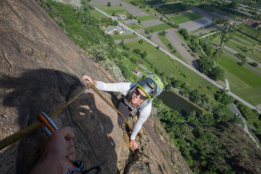 Mature woman ascends via ferrata, valley below