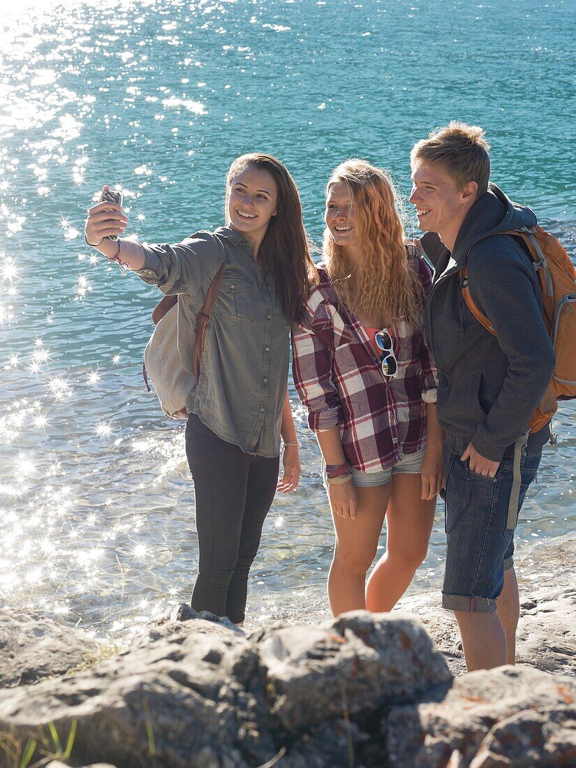 Group of teen hikers take pic with smartphone, mountain lake