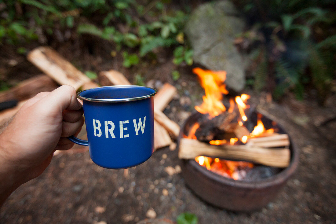 A Camper Enjoying A Mug Of A Beer While Sitting Around A Campfire