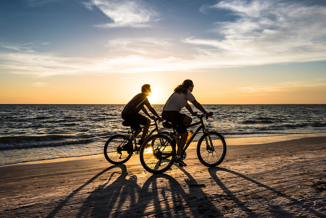 Zwei Radfahrer am Strand zum Sonnenuntergang am Golf von Mexiko, Fort Myers Beach, Florida, USA