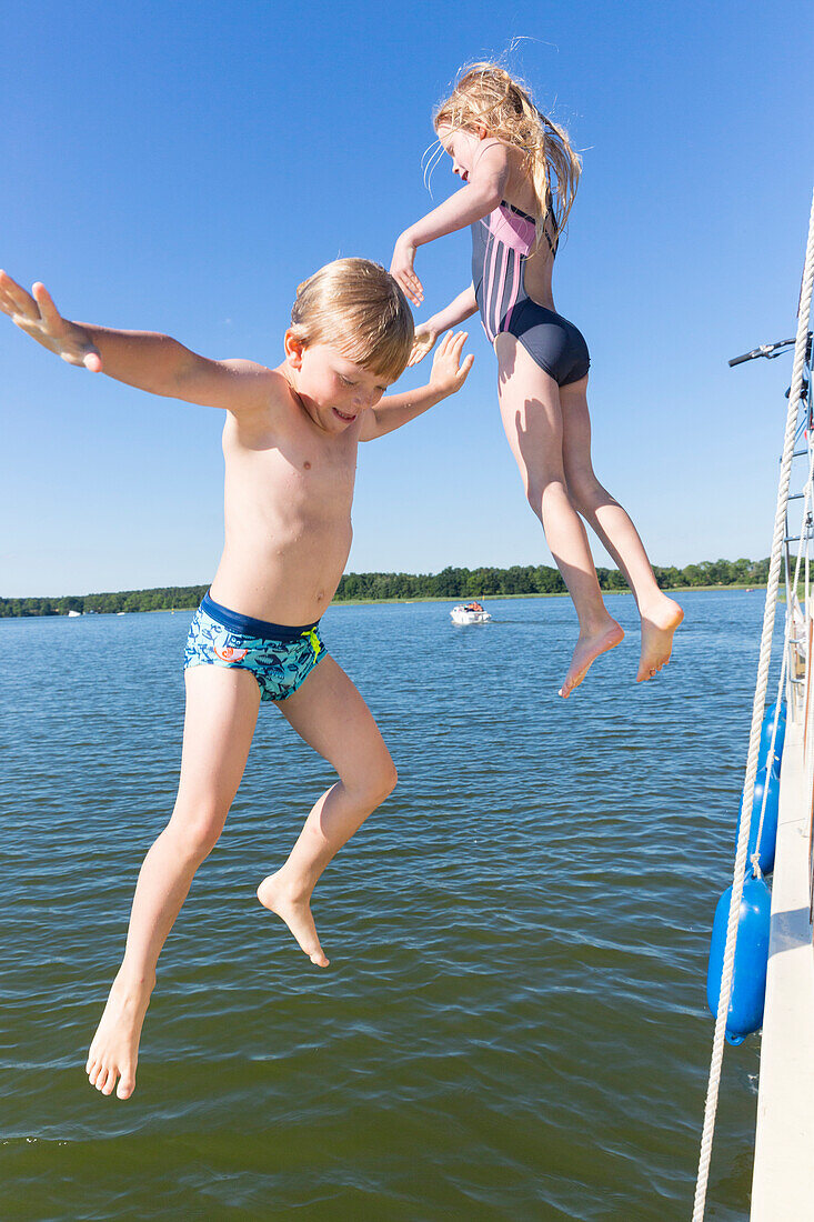 Boy and girl jump from boat into the water, swimming fun with a family, houseboat tour, south of lake Müritz, lake Vilzsee, Kuhnle-Tours, Mecklenburg lakes, Mecklenburg lake district, MR, Mecklenburg-West Pomerania, Germany, Europe