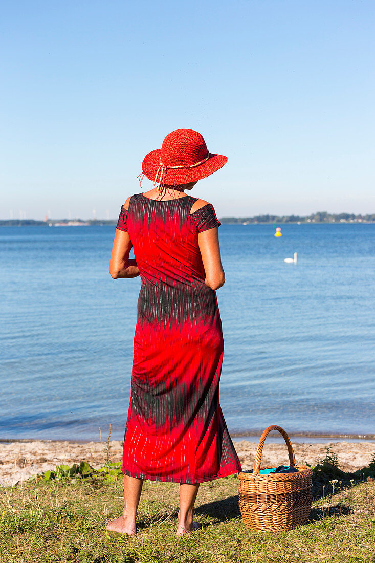 Women with red hat and red dress at lake, basket, lakeshore, beach, swimming spot, near Plau am See, Lenz, Mecklenburg-West Pomerania, Germany, Europe