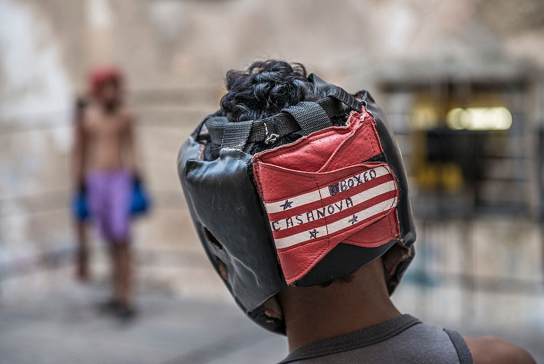 'Closeup of a the head and headgear of a young Cuban boy as he prepares to spar with his opponent seen in the background at Project Cuba Boxeo, an aid project from Malaika Aid for Children, the creation of Samuel 'Sammy' Fabbri. The organization brings bo