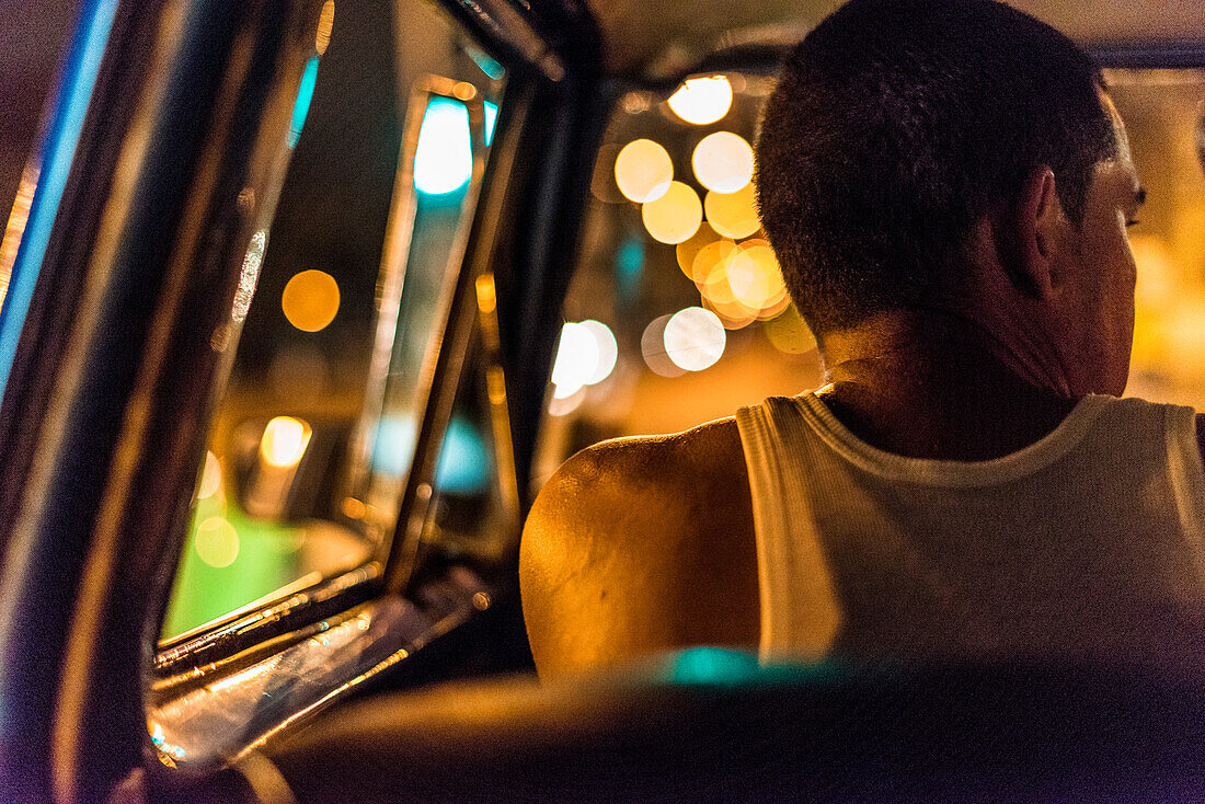 'Inside a Cubanlocals only'' taxi colectivo at night. Because of the two monetary system in Cuba, and although forbidden by the Cuban government, colectivo drivers pick up tourists for payment in CUCs.. The driver wears a tank top, and colorful lights glo