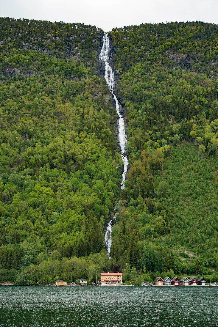 Waterfall cascading down to homes and boat houses along the Sognefjord in Norway