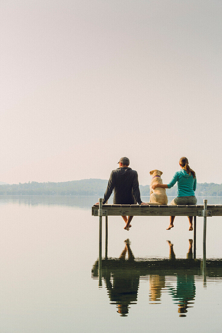 Man And Woman With Their Dog Sitting On Dock On Caspian Lake