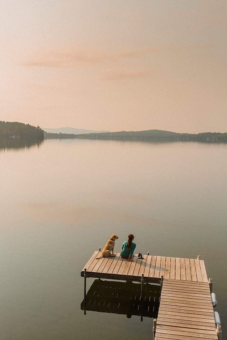 Woman With Her Dog Sitting On Edge Of Dock In Caspian Lake