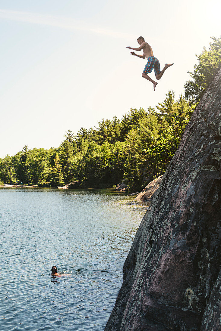 A Young Man Is Jumping Off A Cliff Into George Lake While Another Person Is Looking From Under
