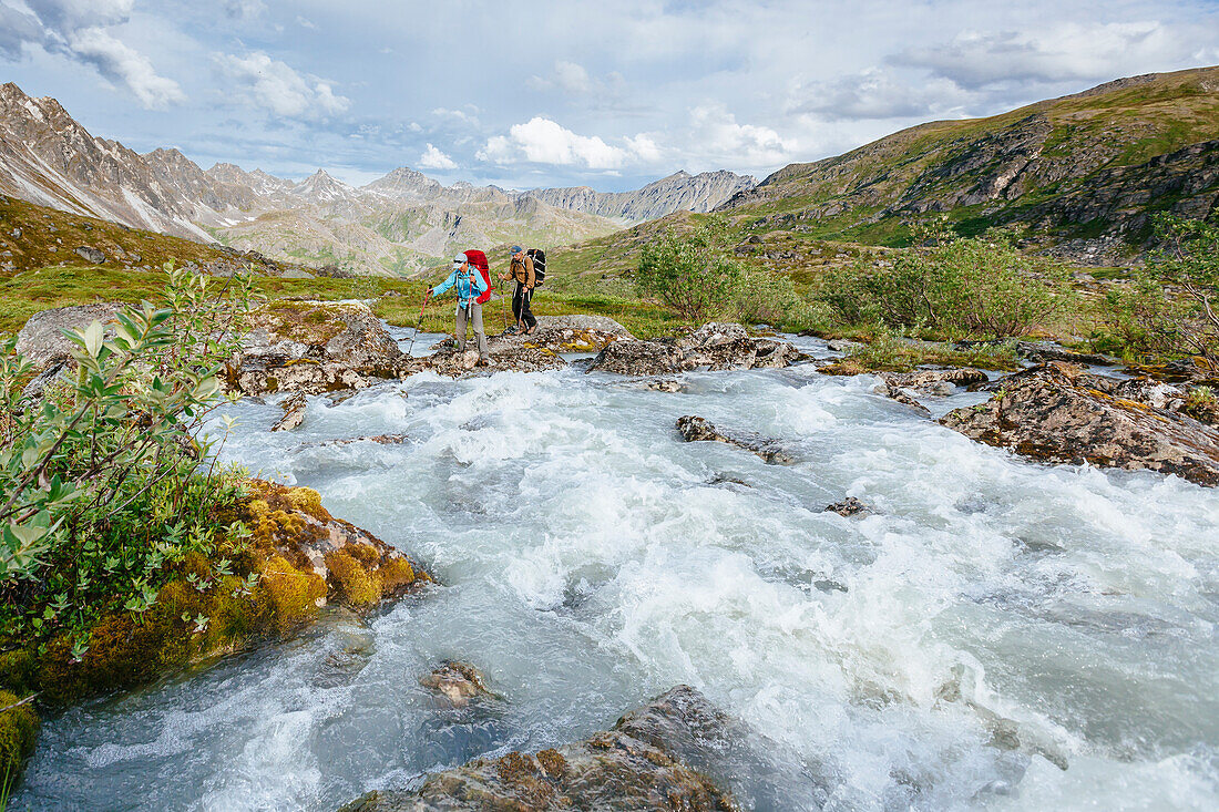 A Man And Woman Crossing A River In Talkeetna Range In Alaska, Usa