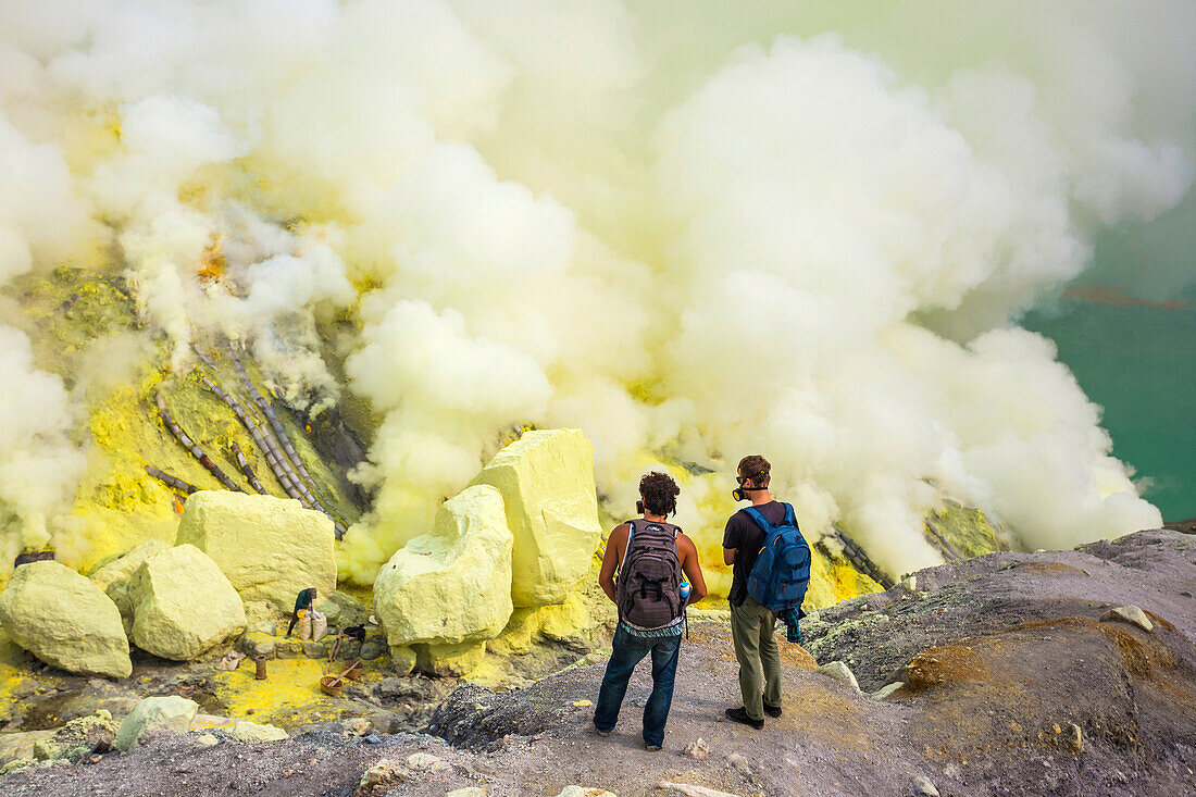 Two Men Exploring Sulfur Dioxide Smoke At Kawah Ijen, Java, Indonesia