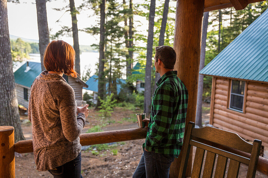 A Young Couple Enjoy An Evening On The Porch Of A Cabin At The Lodge Near Greenville, Maine