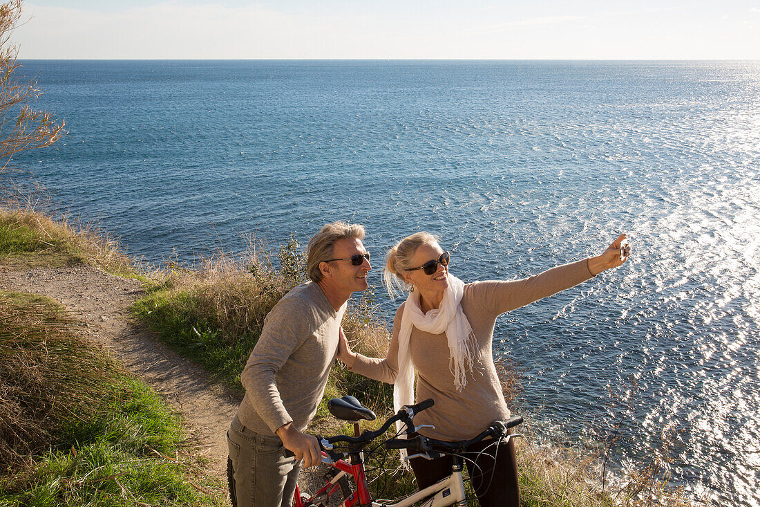 Couple with bikes take selfie above sea