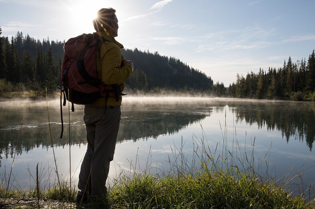 Hiker pauses at edge of mountain lake, sunrise