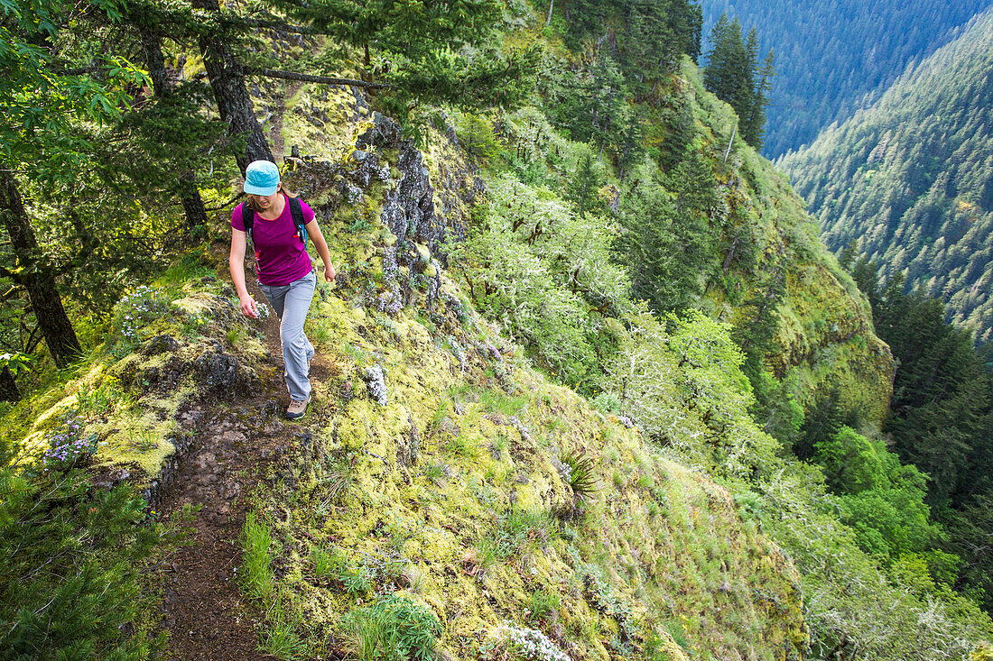 A Woman Walks Up A Narrow Trail With A Steep Drop Into A Green Valley Below