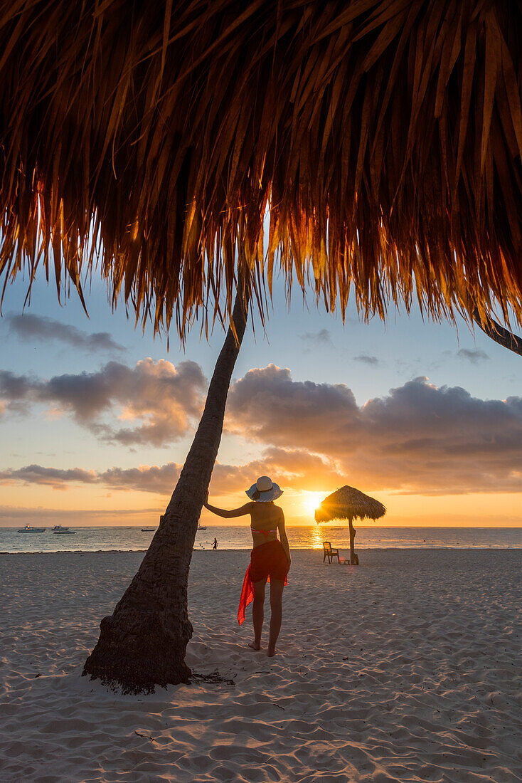 Bavaro Beach, Bavaro, Higuey, Punta Cana, Dominican Republic,  Woman by thatch umbrellas on the beach at sunrise , MR