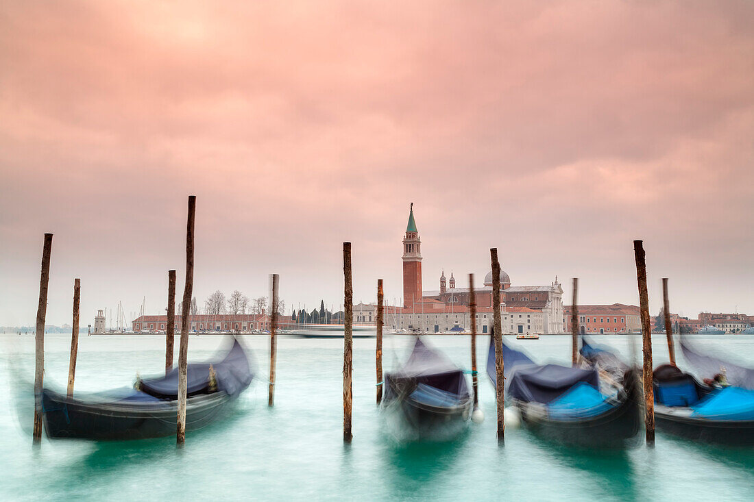 Europe, Italy, Veneto, Venice,  Gondolas tied up to wooden poles on the Canal Grande, in the background the monastery of San Giorgio Maggiore