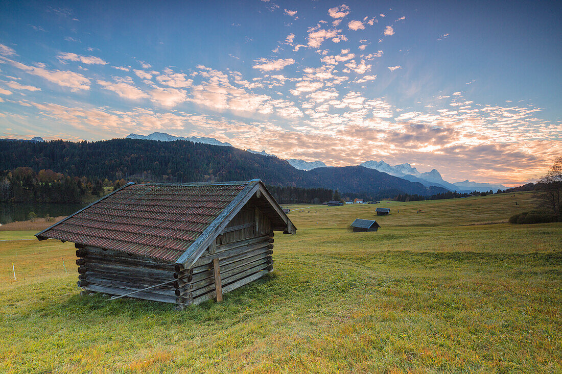 Sonnenuntergang auf Holzhütten und Wiesen mit den Alpen im Hintergrund Geroldsee Krün Garmisch Partenkirchen Oberbayern Deutschland Europa