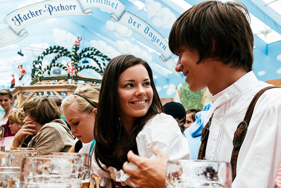Young man and woman in traditional cloth in beer tent at Oktoberfest, Munich, Bavaria, Germany