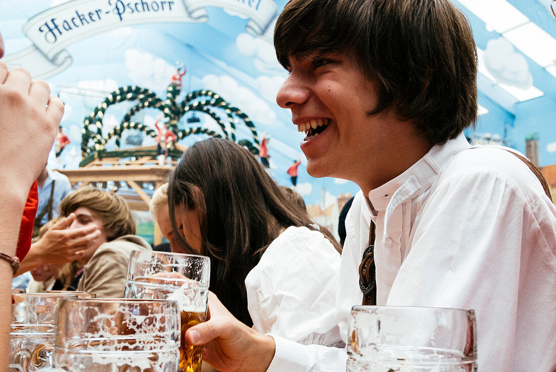 Young laughing man in traditional cloth in beer tent at Oktoberfest, Munich, Bavaria, Germany