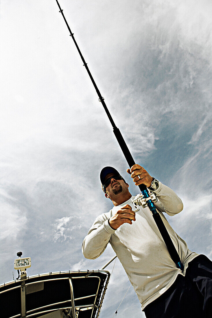 A view looking up at a fisherman holding a fishing pole with wispy clouds in the sky.