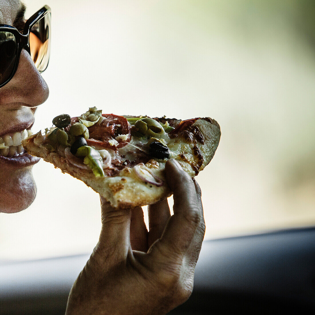 Close up of a woman taking a bite out of a fresh slice of pizza.