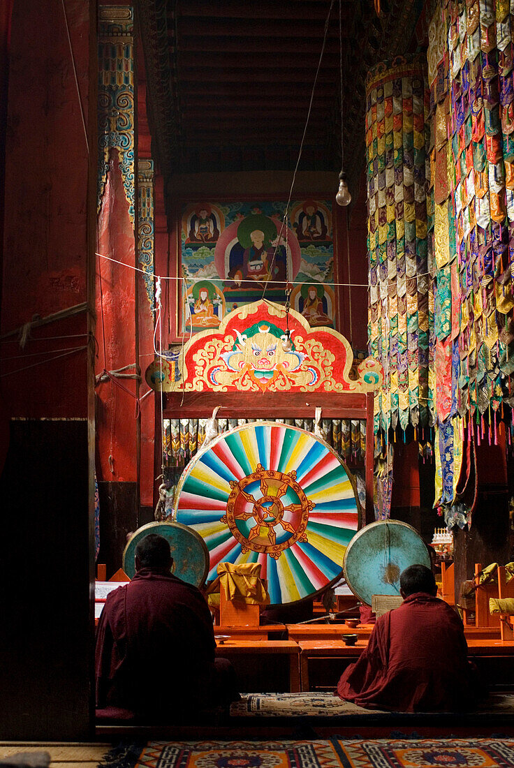 Tibetan Buddhist monks of the Nyingmapa Order sit in front of large, brightly painted drums used during chanting and prayer in the Po Dang Gompa, or Palace Monastery in Sadeng, Tibet Autonomous Region, China.