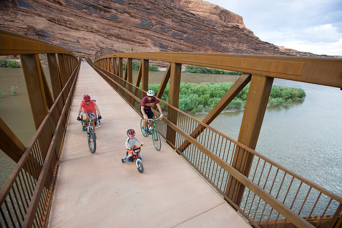 Ashley Korenblat, Mark Sevenoff, and son Kip Sevenoff biking on the pedestrian bridge going over the Colorado river in Moab, Utah.