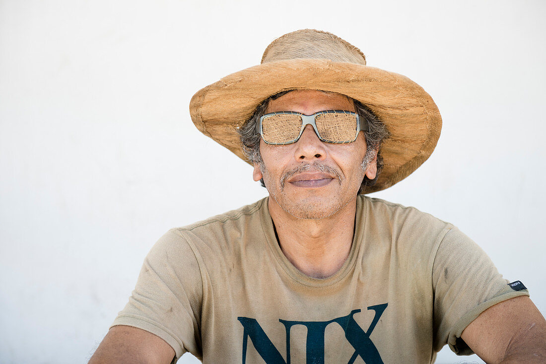 A middle aged mexican man shows off some coconut fiber apparel made by himself, including a hat and sunglasses.