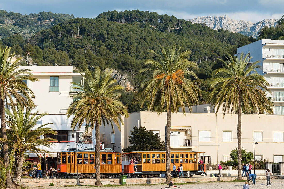 Blick vom Hafen auf die Promenade mit der alten Straßenbahn und dem Tramuntanagebirge im Hintergrund, Port de Sóller, Mallorca, Spanien