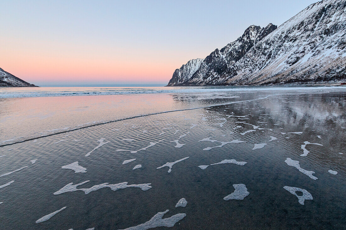 Das rosa Licht des Sonnenaufgangs über die Wellen des kalten Meeres, umgeben von schneebedeckten Gipfeln, Ersfjord, Senja, Troms, Norwegen, Skandinavien, Europa