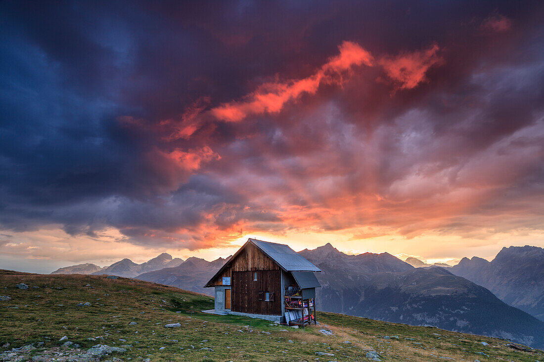Wooden hut framed by fiery sky and clouds at sunset, Muottas Muragl, St. Moritz, Canton of Graubunden, Engadine, Switzerland, Europe