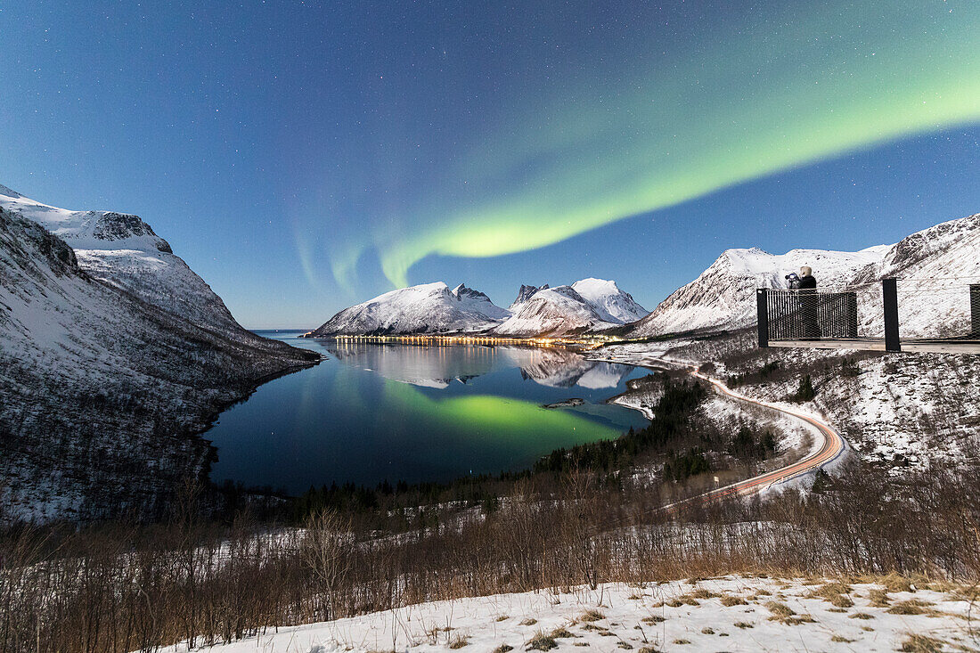 Fotograf auf der Plattform bewundert die Nordlichter (Aurora Borealis) und Sterne spiegelt sich im kalten Meer, Bergsbotn, Senja, Troms, Norwegen, Skandinavien, Europa