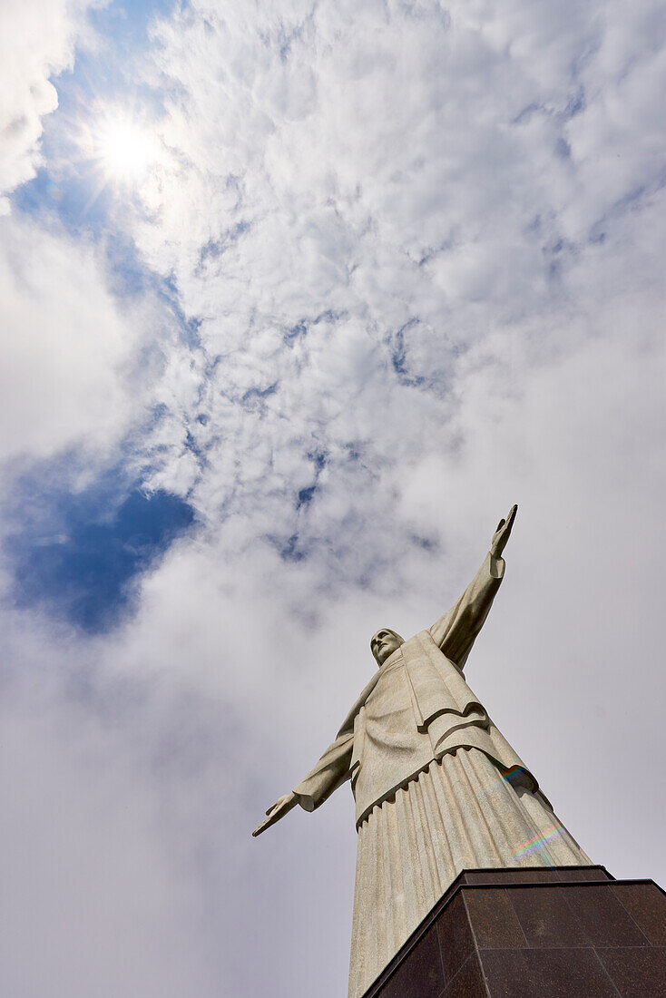 Niedriger Winkel Schuss der ikonischen Statue von Christus der Erlöser an einem bewölkten Tag mit Sonne scheint durch Wolken, Rio de Janeiro, Brasilien, Südamerika