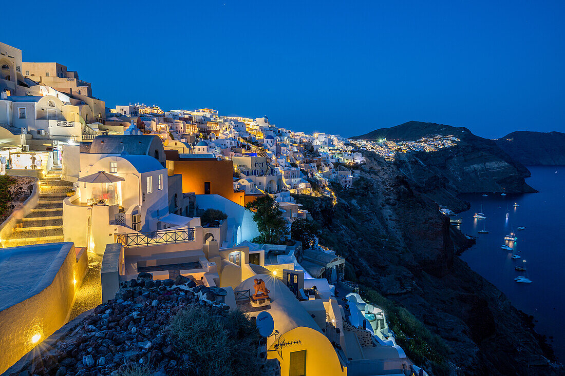The view from Oia castle along Santorini's caldera during the evening blue hour with the buildings lit, Santorini, Cyclades, Greek Islands, Greece, Europe