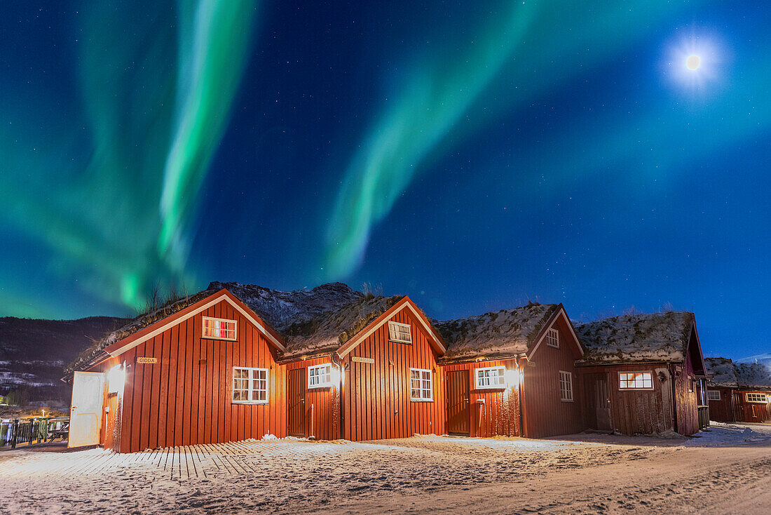Die Nordlichter (Aurora Borealis) und der Mond leuchten typische Holzhütten namens Rorbu, Manndalen, Kafjord, Lyngen Alpen, Troms, Norwegen, Skandinavien, Europa