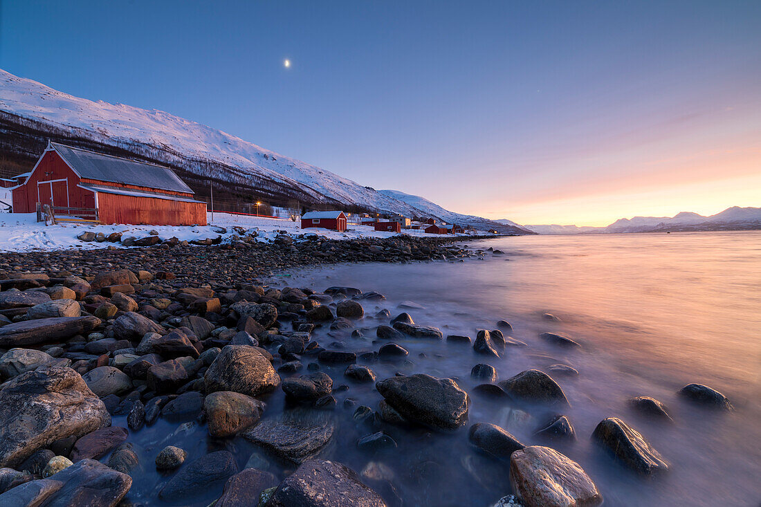 Feuriger Himmel bei Sonnenuntergang und typischen Rorbu, schneebedeckten Gipfeln und gefrorenem Meer, Djupvik, Lyngen Alpen, Troms, Norwegen, Skandinavien, Europa
