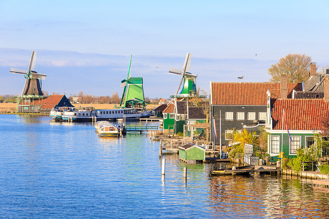 Holzhäuser und Windmühlen spiegeln sich im blauen Wasser des Flusses Zaan, Zaanse Schans, Nordholland, Niederlande, Europa