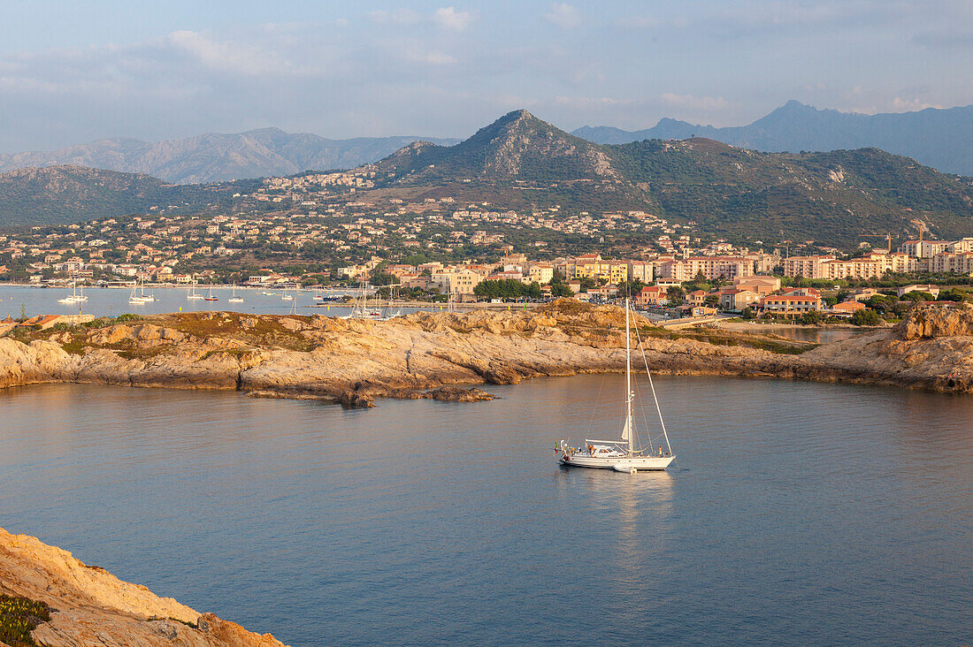 Ein Segelboot im klaren Meer um das Dorf Ile Rousse bei Sonnenuntergang, Balagne Region, Korsika, Frankreich, Mittelmeer, Europa